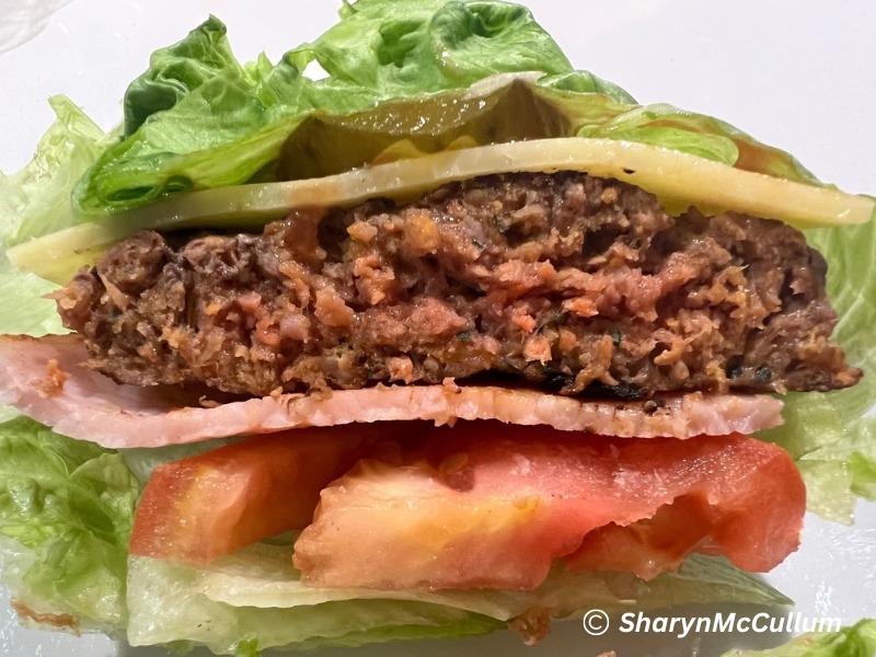 lettuce burger - meat patty, bacon, tomato, cheese, pickles and sauce wrapped in a lettuce leaf.