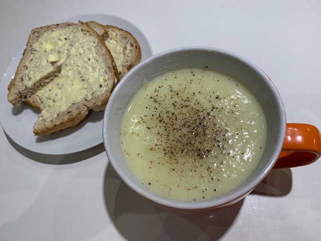 Potato and Leek Soup In A Large Orange Soup Bowl With A Side Of Bread And Butter.