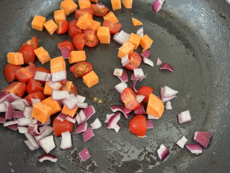cooking chopped onion, tomato and sweet potato in a frypan for breakfast flan.